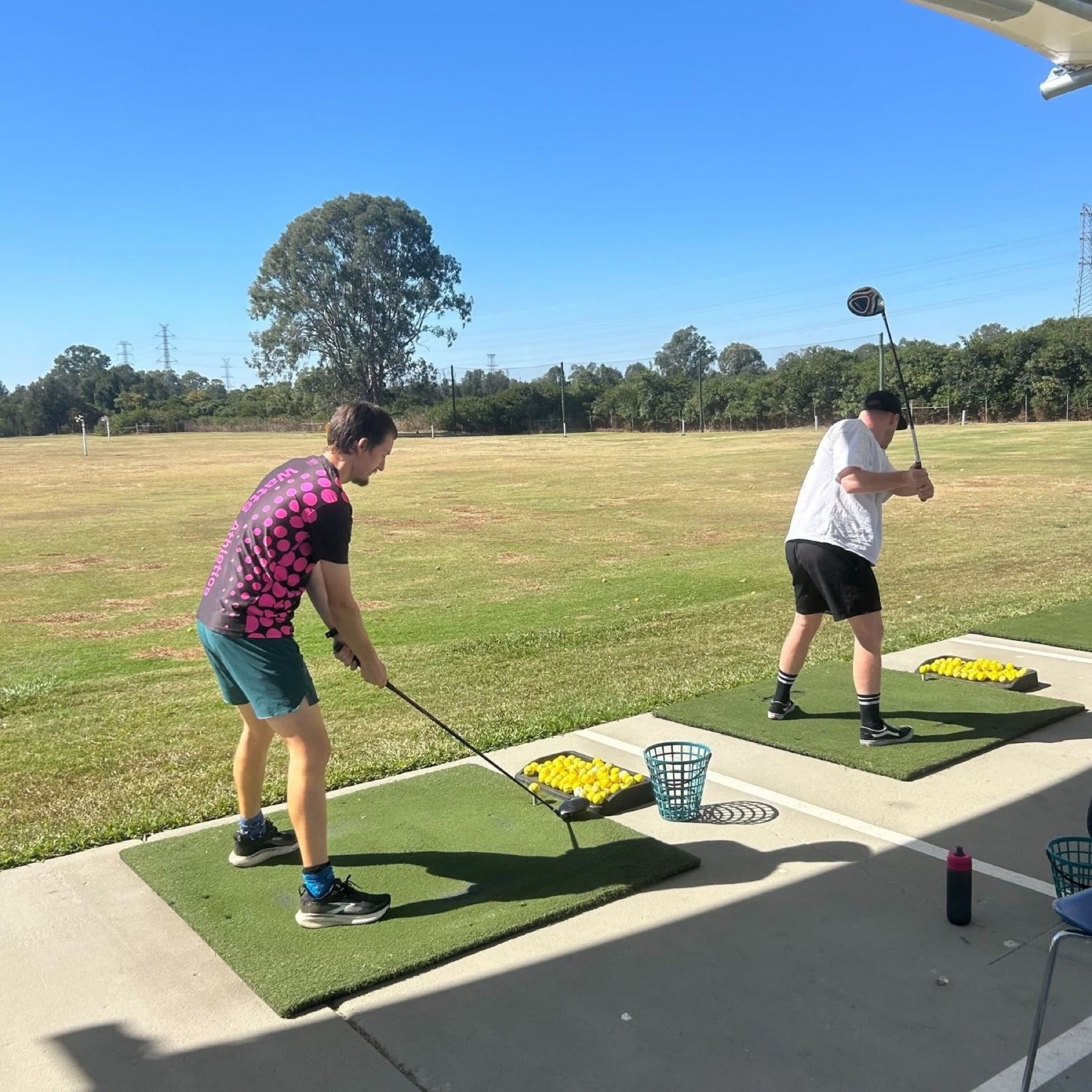 Two people practising golf together at a driving range